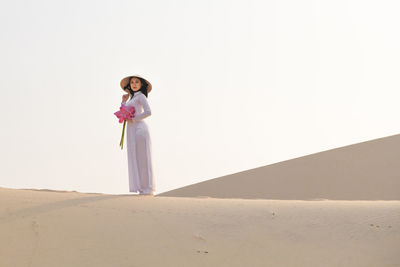 Woman standing on sand dune against sky