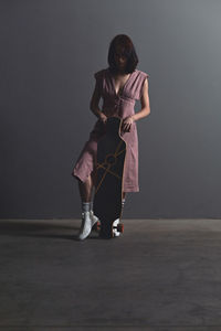 Woman with skateboard standing against wall 