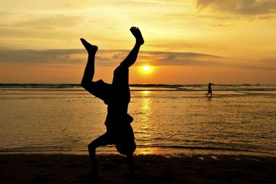 Silhouette man doing handstand at beach against sky during sunset