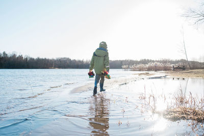 Young boy walking in the water at the beach playing with toys