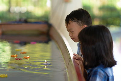 Side view of kids standing by tea light candles in water at temple