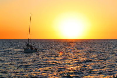 Silhouette sailboat in sea against orange sky