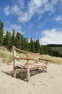 Wooden chair on beach against sky