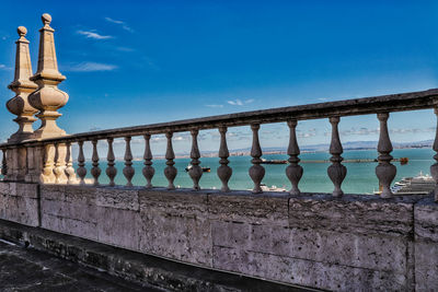 Metal railing by sea against blue sky