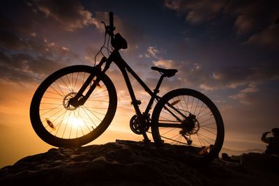 Low angle view of silhouette bicycle on mountain against cloudy sky during sunrise