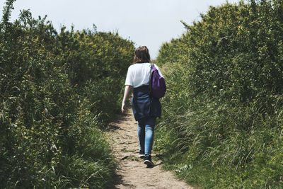 Rear view of woman walking on field against sky