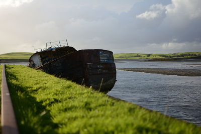 Abandoned boat moored at sea shore against sky