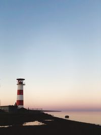 Lighthouse by sea against clear sky