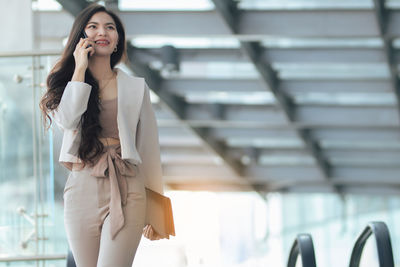 Smiling young woman talking on phone while walking outdoors