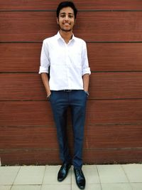 Portrait of young man standing against wooden wall