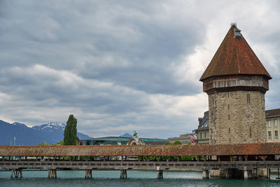 Bridge over river by buildings against cloudy sky