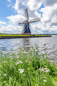 Traditional windmill in lake against cloudy sky