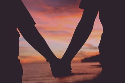 Silhouette couple holding hands on beach at sunset