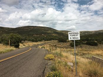 Information sign on road by landscape against sky