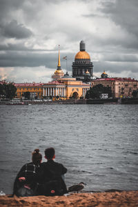 People at waterfront against cloudy sky