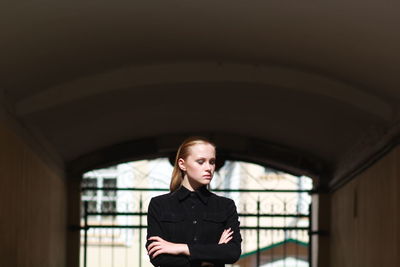 Young woman with arms crossed standing against gate