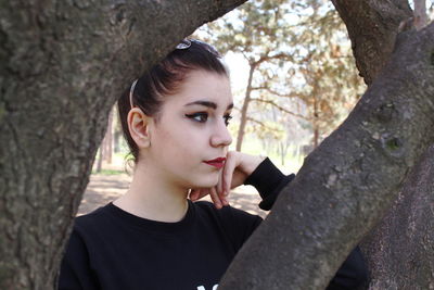 Portrait of beautiful young woman against tree trunk