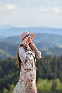 Woman wearing hat and sunglasses while standing against mountain