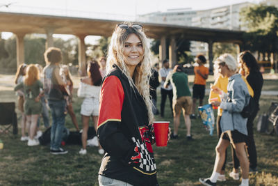 Portrait of smiling woman with drink standing against friends at festival