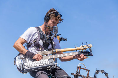 Low angle view of man playing guitar against blue sky