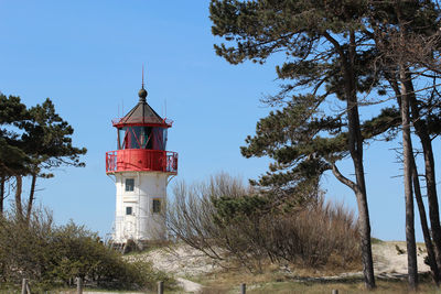 Lighthouse amidst trees and buildings against sky