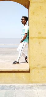 Side view of young man leaning on wall by sea