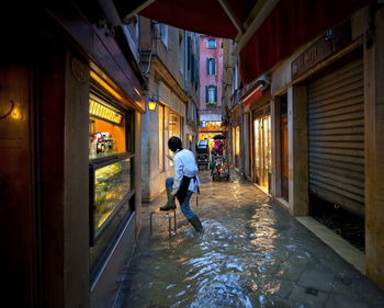 Rear view of sales clerk climbing on stool at water filled alley during flood