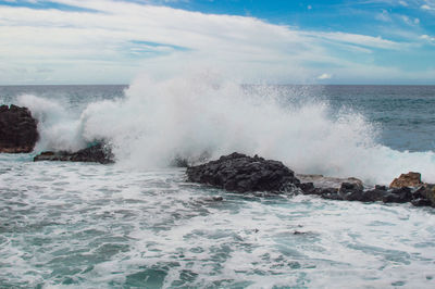 Waves splashing on rocks against sky