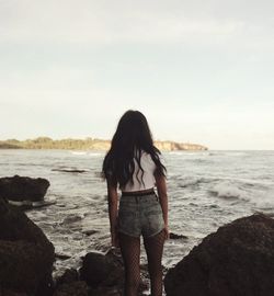 Rear view of woman standing on beach against sky