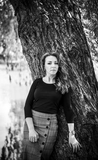 Portrait of woman standing by tree trunk