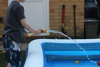 Midsection of boy filling wading pool at yard