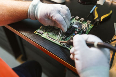 Technician soldering circuit board of electrical component at workbench in electronics repair shop