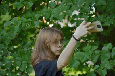 A girl takes pictures of herself on her phone near the trees