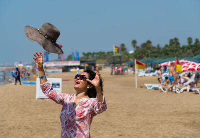 Happy woman catching hat at beach