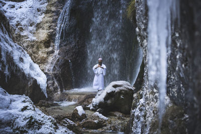 Man standing on rock against waterfall in forest