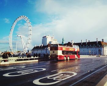 Ferris wheel by road against sky in city