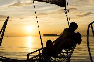 Low section of woman sitting on boat on sea against sky during sunset