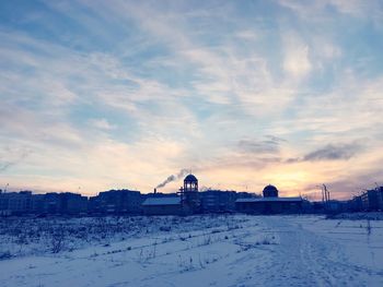 Snow covered city against sky during sunset