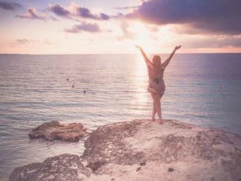 Rear view of woman standing on rock against sea