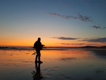 Silhouette man standing on beach against sky during sunset