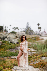 Young pregnant woman posing at beach in sheer dress