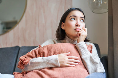 Young woman looking away while sitting on sofa at home