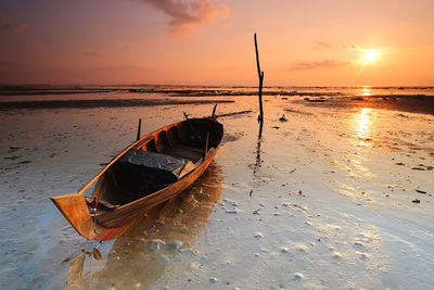 Nautical vessel on beach against sky during sunset