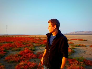 Young man standing at desert against sky during sunset