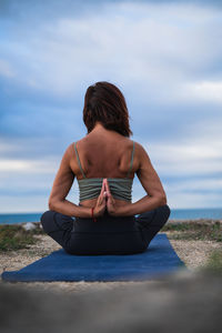 Rear view of woman sitting on beach against sky