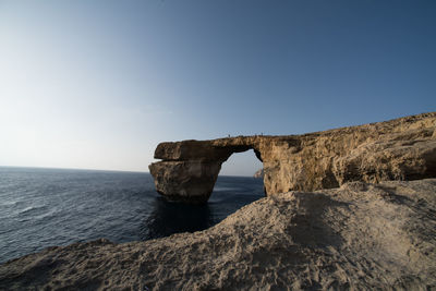 Rock formation by sea against clear sky