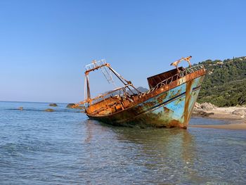 Abandoned ship in sea against clear blue sky