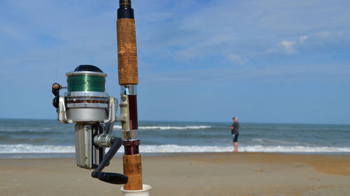 Close-up of fishing rod with man standing in background at beach