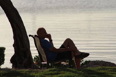 Side view of mature man sitting on chair by lake