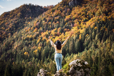 Rear view of woman with arms raised standing in valley surrounded by hills, mountains, autumn, fall.